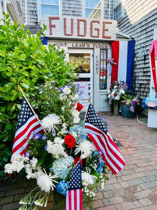 A storefront named "Aunt Leah's Fudge" adorned with flowers and American flags, celebrating a festive occasion.