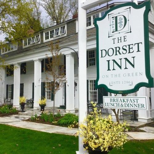 Sign for The Dorset Inn, established in 1796, with a charming white building and greenery in the background.