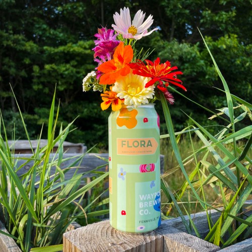 A colorful can of beer filled with fresh flowers, placed on a wooden surface surrounded by greenery.
