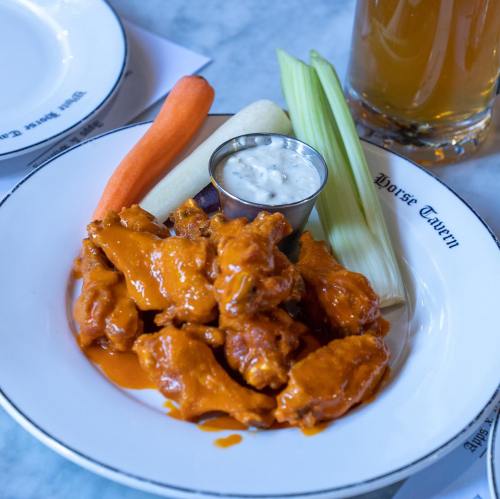 A plate of buffalo chicken wings with celery, carrot sticks, and a small cup of ranch dressing.