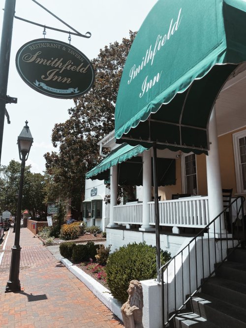 Exterior view of Smithfield Inn, featuring a green awning, sign, and brick pathway lined with plants.