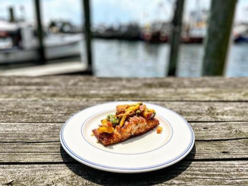 A slice of pizza topped with vegetables on a white plate, set on a wooden table by a waterfront.