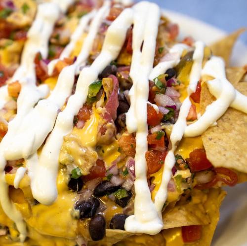 A close-up of nachos topped with melted cheese, black beans, diced tomatoes, and drizzled with sour cream.