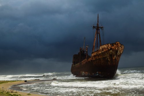 An abandoned, rusted ship stranded on a beach under a dark, stormy sky with crashing waves.