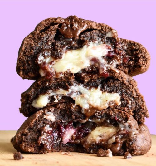 Three stacked chocolate cookies filled with gooey cheese and berry jam, set against a pastel purple background.