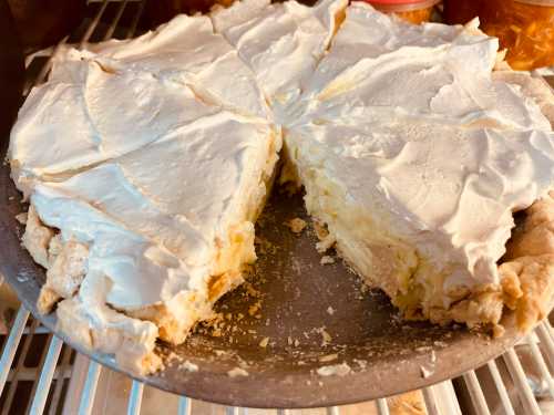 A partially sliced cream pie with a fluffy white topping, sitting on a metal pie dish in a refrigerator.