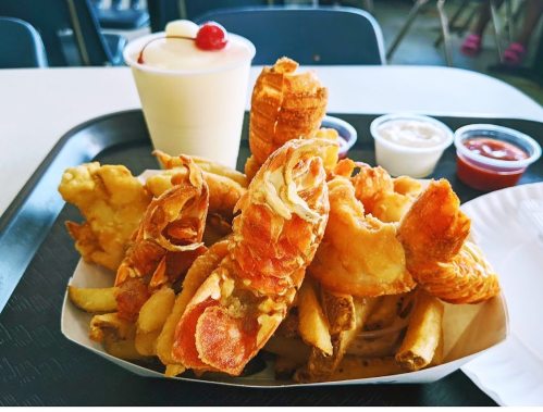 A tray with crispy fried shrimp, French fries, and dipping sauces, alongside a dessert cup topped with a cherry.