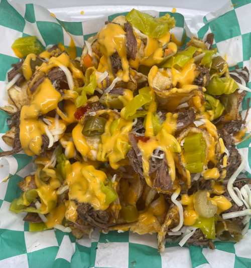 A plate of nachos topped with melted cheese, shredded beef, jalapeños, and green peppers on a checkered paper background.