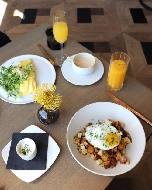 A brunch spread featuring an omelette, potatoes with an egg, salad, and drinks on a wooden table.