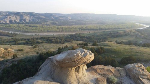 A scenic view of rolling hills and a river, with a unique rock formation in the foreground under a clear sky.