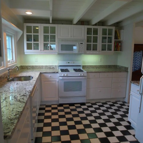 Bright kitchen with white cabinets, granite countertops, a gas stove, and a checkered black-and-white floor.