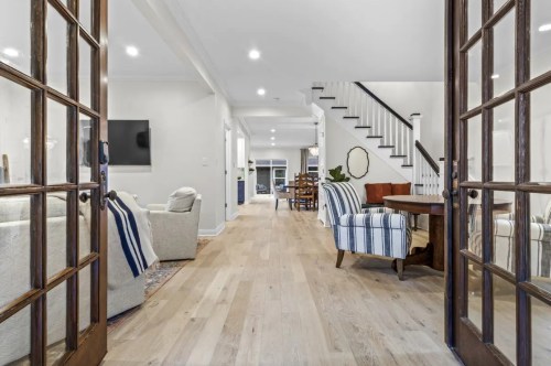 A bright, open hallway with wooden floors, leading to a living area and dining space, framed by glass doors.