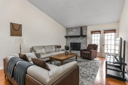 Cozy living room with a stone fireplace, comfortable seating, and a wooden coffee table, featuring natural light from windows.