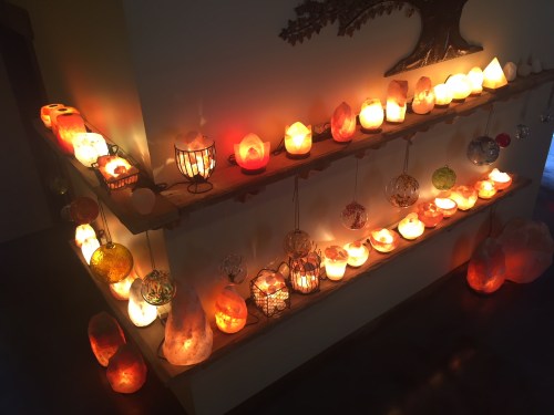 A cozy display of glowing salt lamps and decorative candles on wooden shelves, creating a warm ambiance.