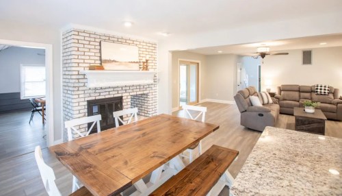 Bright, open living space featuring a wooden dining table, cozy seating area, and a brick fireplace.