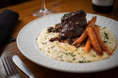 A plate of tender beef with carrots on creamy mashed potatoes, garnished with herbs, set on a wooden table.