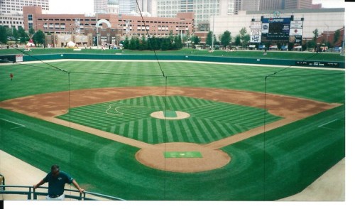 A panoramic view of a well-maintained baseball field with a city skyline in the background.