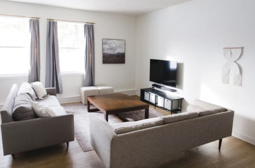 A modern living room with two sofas, a coffee table, a TV, and large windows with gray curtains.