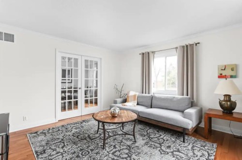 Bright living room with a gray sofa, round coffee table, and large window, featuring a patterned rug and light curtains.