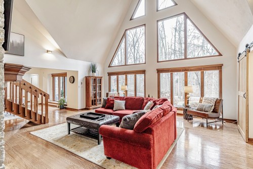 Spacious living room with large windows, a red sofa, wooden floors, and a cozy reading nook.