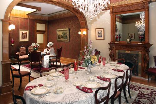 Elegant dining room with a beautifully set table, vintage decor, and a woman in a white hat seated in the background.