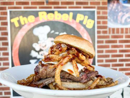 A hearty sandwich with beef, melted cheese, crispy onions, and barbecue sauce, served on a bun against a colorful backdrop.
