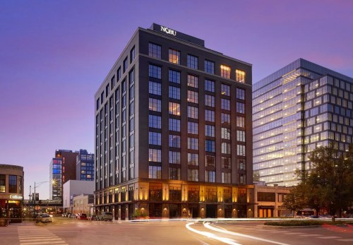 Modern hotel building at dusk, featuring large windows and a sleek design, surrounded by city skyscrapers.