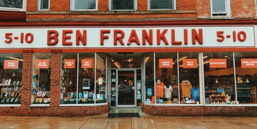 A storefront of Ben Franklin 5-10, featuring colorful signage and a variety of merchandise displayed in the windows.