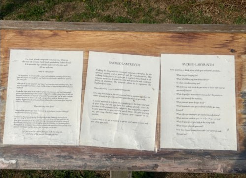 Three informational plaques on a wooden surface, discussing the concept and purpose of a sacred labyrinth.
