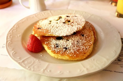 Two fluffy pancakes dusted with powdered sugar, served with a fresh strawberry on a decorative plate.