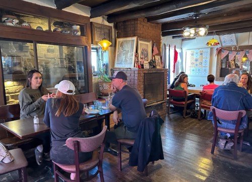 A cozy restaurant interior with patrons at tables, featuring rustic decor and warm lighting.