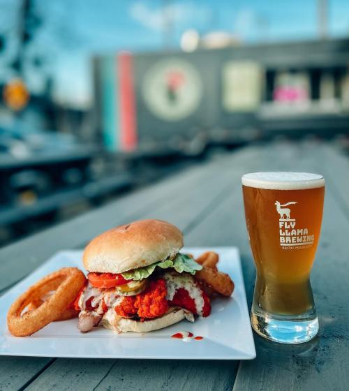 A crispy chicken sandwich with lettuce and sauce, served with onion rings and a glass of beer on a wooden table.