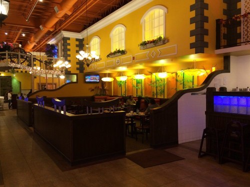 Interior of a vibrant restaurant with yellow walls, decorative lighting, and wooden seating arrangements.