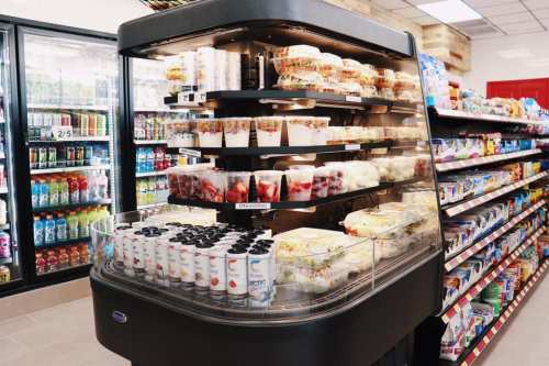 A refrigerated display case filled with salads, yogurt, and desserts, surrounded by shelves of beverages.