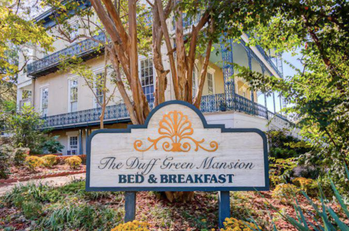 Sign for The Duff Green Mansion Bed & Breakfast, surrounded by lush greenery and colorful flowers.