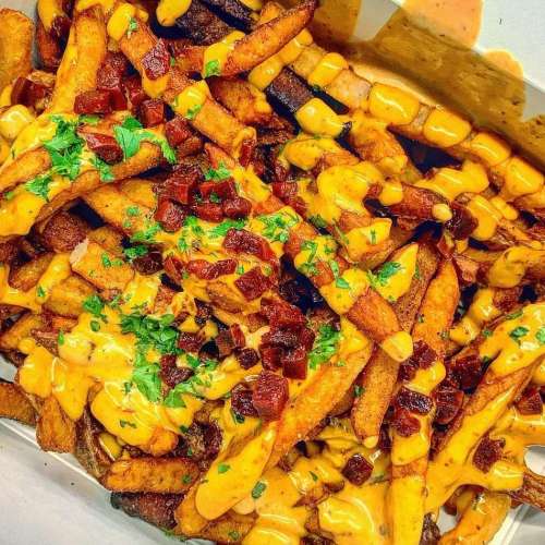A close-up of crispy fries topped with cheese sauce, chopped bacon, and fresh parsley.