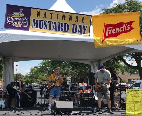 A band performs on stage at the National Mustard Day festival, with banners for French's and the Mustard Museum above.