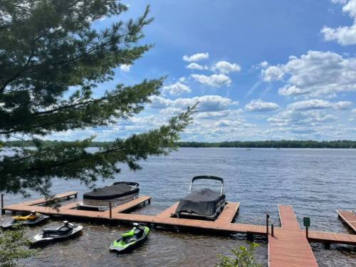 A serene lake view with wooden docks, boats, and a clear blue sky dotted with fluffy clouds.