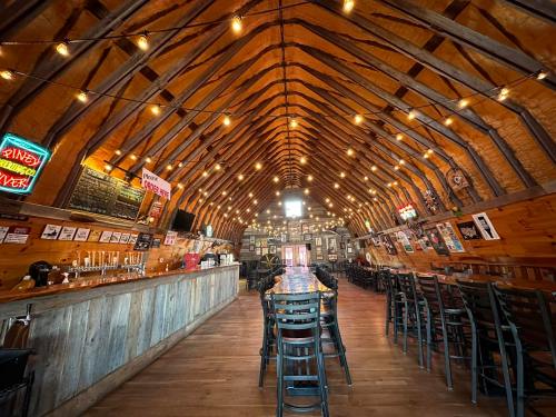 Interior of a rustic restaurant with wooden beams, a long table, bar area, and warm string lights.