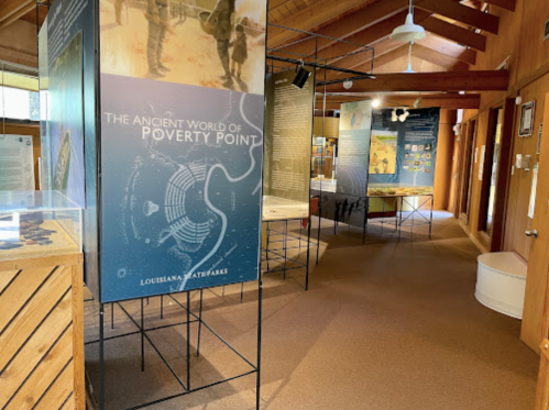 Interior of a museum exhibit featuring displays about Poverty Point, with informational panels and wooden structures.