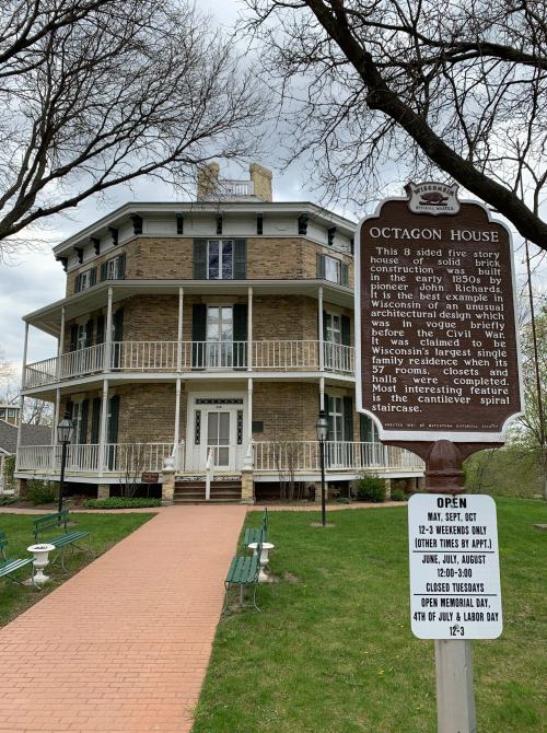 Historic Octagon House, a six-sided stone building with balconies, surrounded by greenery and a sign detailing its history.