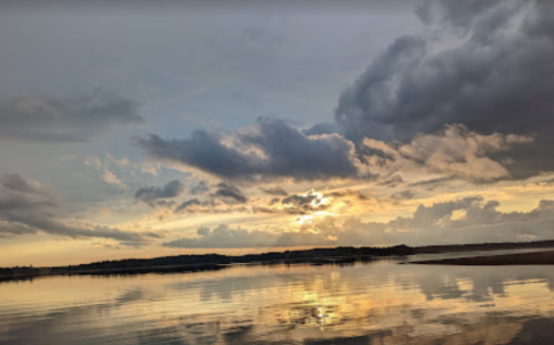 A serene sunset over a calm lake, with clouds reflecting on the water's surface.