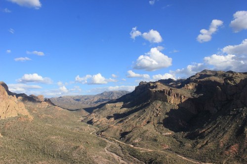 A scenic view of rugged mountains and a valley under a blue sky with fluffy clouds.