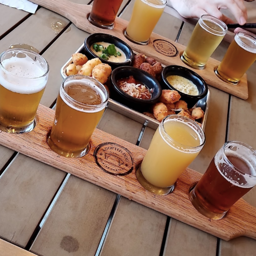 A wooden flight of craft beers alongside a platter of appetizers on a table.
