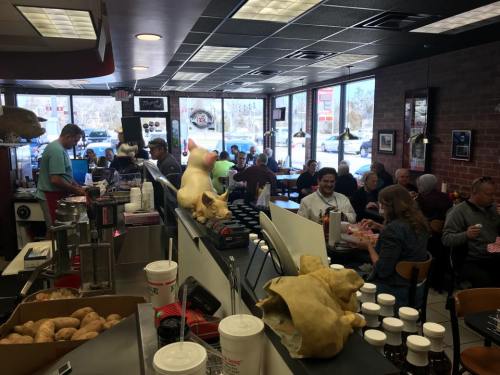 A busy diner with patrons enjoying meals, a cook at the grill, and a view of the street through large windows.