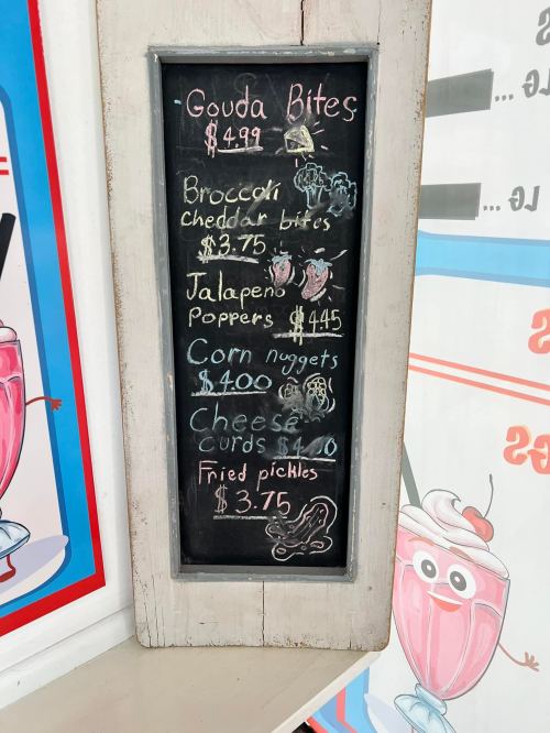 Chalkboard menu listing snacks: Gouda Bites, Broccoli Cheddar Bites, Jalapeno Poppers, Corn Nuggets, Cheese Curds, Fried Pickles.