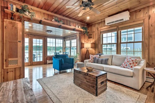 Cozy wooden living room with a white sofa, blue chair, and large windows overlooking a scenic view.