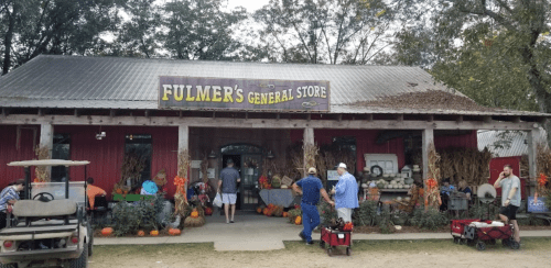 A rustic general store with pumpkins outside, people shopping, and autumn decorations.