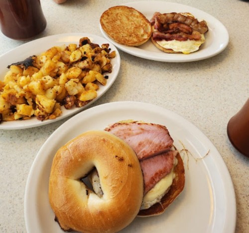 A plate with a bagel sandwich filled with ham and cheese, alongside a breakfast sandwich and a side of crispy potatoes.