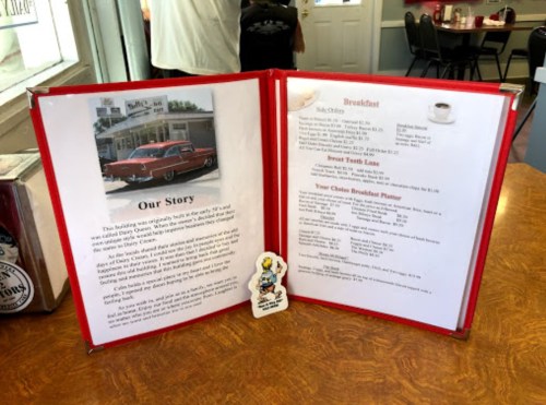A menu open on a table, featuring a story about the building and breakfast options, with a vintage car photo.